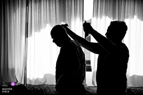  A groomsman with the groom getting ready at Villa La Selva in Tuscany, offering help and support, their camaraderie shining during a key moment of the wedding day.