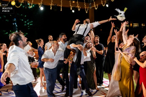 Friends Lift Each Other To Grasp The Bouquet During Traditional Toss At Kemer Country Club, Istanbul, Turkey. Guests crowd around, lifting one friend onto shoulders to grasp the flying bouquet tossed by the bride at Kemer Country Club, Göktürk, Istanbul, turning tradition into a spirited contest.
