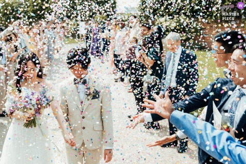 Guests Celebrate Amid Bursts Of Color And Laughter As Confetti Flies Over Newlyweds At The Walled Garden, Nottingham. Confetti flies in a colorful, wild flurry over the couple at The Walled Garden, Nottingham, UK, with guests celebrating the newlyweds amid bursts of color and laughter.