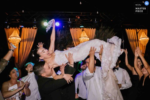 At Four Seasons Hotel In Istanbul, The Bride Laughs With Delight While Being Lifted During A Memorable Group Dance. The bride, elevated in arms at the Four Seasons Hotel in Istanbul, laughs with delight as loved ones watch during a playful and memorable dance.