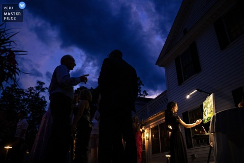   During the dusk cocktail hour at The Barrows House in Dorset, Vermont, guests chat and sip drinks outdoors while an artist adds finishing touches to a portrait of the couple from earlier in the day.