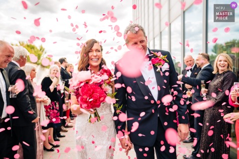   At Turner Contemporary in Margate, Kent, the newlyweds walk through a flutter of vibrant pink confetti, surrounded by cheering guests under the contemporary gallery's dramatic architecture.