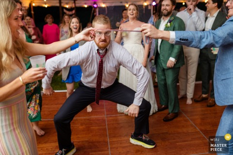   During the celebration at Highland Lodge in Greensboro, Vermont, a male guest eagerly prepares to limbo on the dance floor, adding energy and excitement to the wedding festivities.