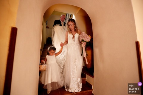 Walking Away From Her Childhood Home In Ciminà, Calabria, The Bride’s Journey To Church Begins With A Little Companion. Departing her family home in Ciminà, Calabria, the bride steps down with small girl to travel to the church, marking the beginning of her journey to the wedding ceremony.