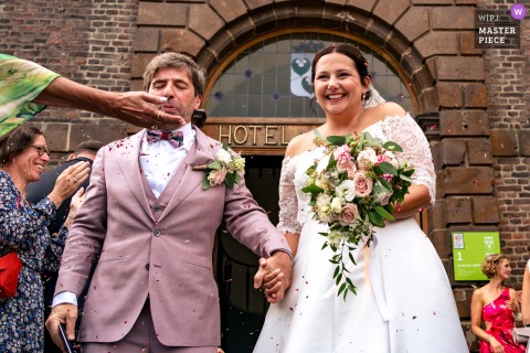   When leaving the church in Wavre, Belgium, a hand holding flowers appears under the groom’s chin, captured in a charming detail as the newlyweds step outside the church.