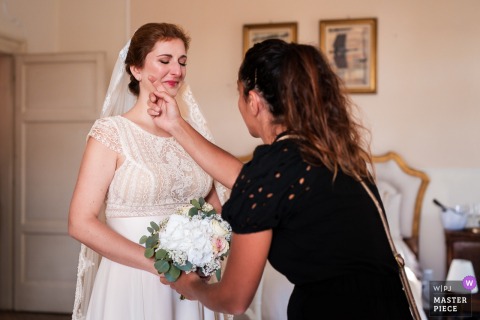   In Gorizia, Italy, the bride is visibly moved as her wedding planner gently wipes away her tears, offering comfort and support during a touching, emotional moment on her special day.