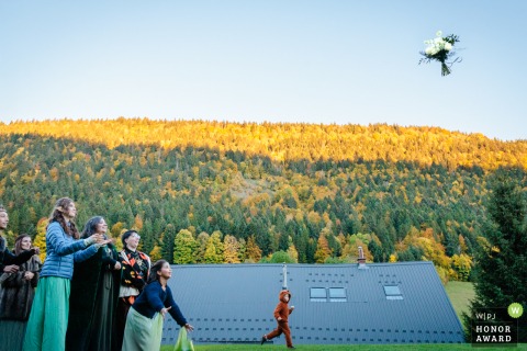 A bridal bouquet soars gracefully through the air at La grange aux fées in Autrans, France, as guests eagerly await to catch it during this joyful tradition.