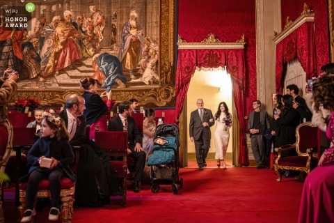 Arriving at Florence's wedding room, the bride steps inside the ceremony location, with guests and architecture creating captivating layers to this striking entrance.