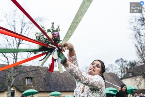   During the ribbon round at Domaine de Rebetz in Hauts-de-France, the bride focuses on cutting the ribbons, taking part in a charming wedding tradition surrounded by guests.