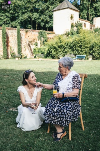   At Domaine de Montchevreuil in Hauts-de-France, the bride shares a gentle moment with her grandmother, exchanging a tender gesture that highlights family bonds on her wedding day.