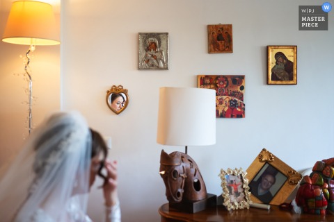   As the bride is about to leave her house in Sardinia, her face is thoughtfully framed between wall and table decorations, capturing her anticipation and the surrounding details just before departure.