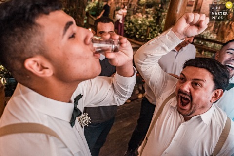   At Canto Verde in São Paulo, Brazil, guests cheer as a man participates in a lively drinking game involving the groom's tie, adding a spirited and playful touch to the festivities.