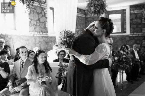 As The Bride Arrives At Borgo Colle Mentuccia, Roma, She Emotionally Embraces Her Groom With Delighted Guests Watching. At Borgo Colle Mentuccia in Roma, the bride, freshly arrived at the ceremony, embraces the groom with emotion, while happy and moved guests look on in the background.