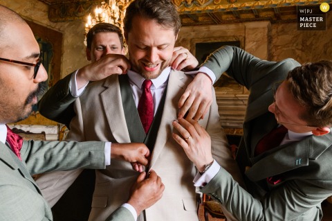 Within Château de Mauriac’s Historic Walls In France, The Groom Prepares For His Wedding Amid Anticipation And Charm. At Château de Mauriac, the groom prepares with help for the big day, carefully getting ready in a space filled with anticipation and the historic charm of the French venue.