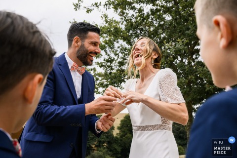 At Maison De Lacan, The Bride And Groom Experience An Awkward Yet Intimate Exchange While Putting On Wedding Rings. At Maison de Lacan, the bride and groom share an intimate and slightly awkward moment as they try to put on the wedding rings during their ceremony, symbolizing their union.