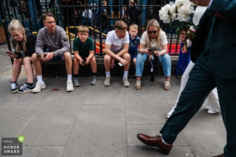 In Marylebone, London, a newly married couple walks past a group of uninterested bystanders on the street, adding a whimsical note to city wedding scenes.