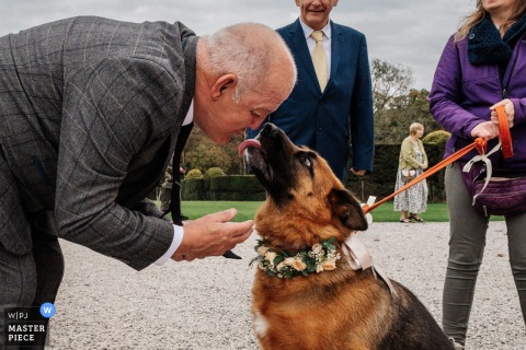   At Kinmount House in Scotland, a humorous moment unfolds as the father of the bride pretends to kiss a dog, delighting everyone and adding playfulness to the wedding celebrations.