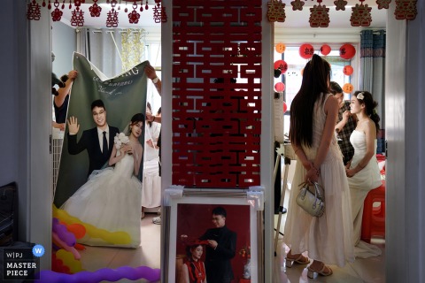   While the bride puts on makeup at home in Shanxi, her friends tidy up the wedding display rack nearby, with wedding photos cleverly displayed between the two bustling rooms.