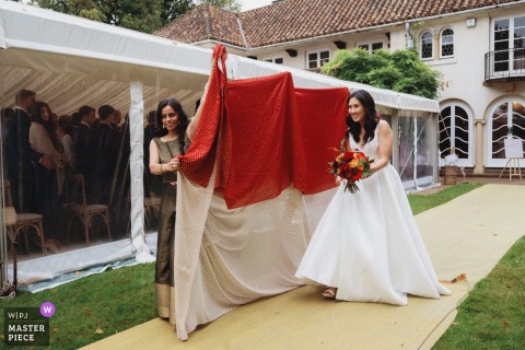  The hidden bride gracefully arrives for the ceremony behind sheets in a private garden in Birmingham, UK, her presence marking the beginning of a special and memorable wedding celebration.