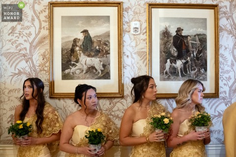 Bridesmaids dressed for a Cambodian wedding wait in front of vintage paintings, standing in anticipation as the ceremony is about to begin.