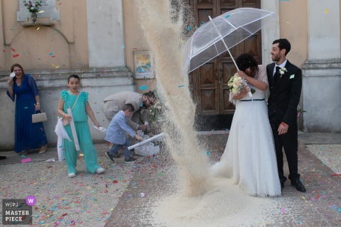 Outside the parish of San Prospero in Suzzara, Mantova, Italy, a heavy rain of rice falls over the newlyweds, scattering surprise and laughter across the ceremony.
