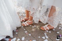 Graceful Steps on a Confetti-Strewn Pathway: The Beauty of a Wedding Day White dresses and ladies' feet in white sandals gracefully walk on a stone pathway scattered with confetti, capturing the beauty of a wedding day