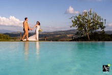 Hand in Hand at Belpoggio: Umbrian Hills Wedding Bliss Bride and groom walk hand-in-hand by a pool at Belpoggio Su Todi, with the Umbrian hills in the background.