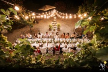 Guests Toast Newlyweds Amid Lush Terraced Vegetation at Farmhouse in Umbria At the groom's sister's farmhouse in Umbria, a wide-angle shot from above captures guests at the table toasting with the newlyweds. The scene is framed by the lush vegetation of the terrace, adding a natural and intimate atmosphere to the celebration.