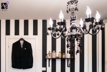 In Trieste, Italy, the groom's suit hangs neatly on a door, with a chandelier in the foreground adding an elegant touch to the preparation scene.