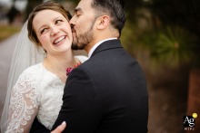 At St. Patrick Roman Catholic Church in Colorado Springs, Colorado, the groom kisses the bride’s neck as they share sweet laughter, capturing an intimate and joyful exchange.