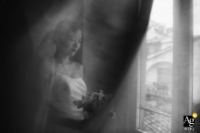 A serene black and white portrait of a bride in a Tuscan hotel, looking at her wedding bouquet by a window.