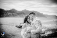 Newlyweds share an intimate embrace by Lake Garda, with serene mountains and water behind them.