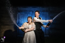 Stratton Court Barn: Backlit Bride and Groom with Blue Light During Champagne Spray Bride and groom lit during a champagne spray at Stratton Court Barn, with a blue gel light behind them.