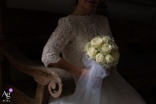 A close-up artistic portrait in Guastalla, Reggio Emilia, Italia, captures the bride's exquisite wedding bouquet and the delicate lace detail of her bodice as she sits in perfect light before leaving.
