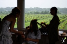 A bridesmaid is silhouetted against the scenic vineyard landscape of Saltwater Farm Vineyard in Stonington, Connecticut, as she has her hair styled before the wedding ceremony begins. 