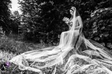 In a garden setting, the bride is seated on a bench with her veil draped elegantly around her as she holds her floral bouquet, creating an artistic portrait on her wedding day.