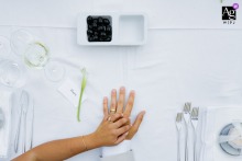 A couple's hands rest gently on a white-linened table in Amares, the bride's atop the groom's, surrounded by the subtle geometry of fine flatware.