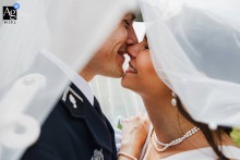 Metz, Moselle — In a tight shot beneath the bride’s veil, she and her husband in military uniform stand in profile, faces nearly touching and smiling radiantly, about to kiss in a tender wedding portrait.