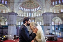 Blue Mosque, Istanbul, Türkiye — In a symmetrically framed wedding portrait, the groom kisses the bride’s head as they stand in profile, with the historic arches and domes of the Blue Mosque providing a dramatic old-world backdrop.