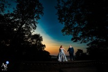 Lauxmont Farms, Sunken Gardens — The couple walks along a wall at sunset, boldly lit by the photographer and framed by dark silhouetted trees, creating a dramatic and striking wedding portrait.