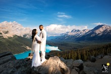 Peyto Lake — The bride and groom, both dressed in all white, share a hug against the stunning backdrop of Peyto Lake and surrounding mountains, lit by the photographer for an unforgettable wedding portrait.