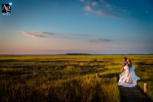 The Sperlak Gallery in Cape May, NJ, provides the backdrop as the bride and groom stand artfully silhouetted at the end of a pier during golden hour over the serene Cape May wetlands.