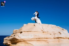 In Rodalquilar Almería Spain Couple Stands on Large Rock by Sea With Dress Blowing Rodalquilar, Almería, Spain — The couple stands atop a large rock by the sea, her dress blowing in the wind, creating a dramatic and scenic wedding portrait along the rugged coastline.