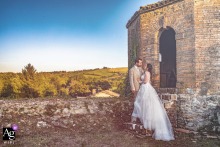 A wedding couple stands close together against the rolling Emilia-Romagna hills, creating a romantic portrait at sunset outside the historic Castello del capitano delle artiglierie in Castrocaro, Italy.