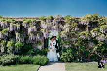 North Cadbury Court, Dorset — The couple stands together among blooming wisteria at North Cadbury Court, creating a romantic and colorful wedding portrait in the venue’s lush gardens.