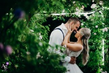 Kingscote Barn, Tetbury — The bride and groom stand face to face under an illuminated rose arch at night, about to kiss, surrounded by lush green foliage in a romantic wedding portrait.