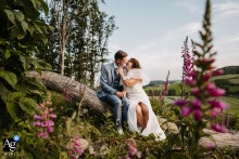 Monts du Lyonnais Couple Shares Kiss on Tree Trunk Surrounded by Wildflowers Monts du Lyonnais — The couple shares an intimate session, sitting and kissing on a downed tree trunk, surrounded by wildflowers, capturing a romantic and natural wedding portrait in the countryside.