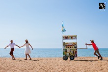 Plage Anglet — The couple runs hand in hand across the sand with a beignet vendor pushing his cart behind them, capturing a joyful and playful wedding portrait on the beach.