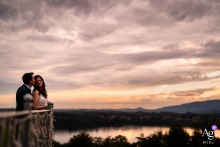 Lake Como Sunset: Villa Dolceacqua's Minimalist Portrait, Newylweds Beneath Dramatic Clouds Villa Dolceacqua, Oggiono, Lake Como, Italy — The newlyweds pose in a minimalist sunset portrait, positioned low in the bottom left corner with a sweeping lake view and dramatic clouds filling the sky above them.