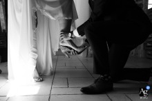   Inside Château des Anglades in Hyères, France, the best man helps the bride put on her shoes, highlighting a tender and supportive wedding day detail.